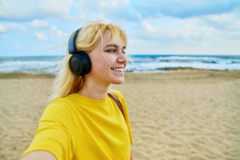 Close-up of happy face of teenage blonde in headphones on the beach, copy space